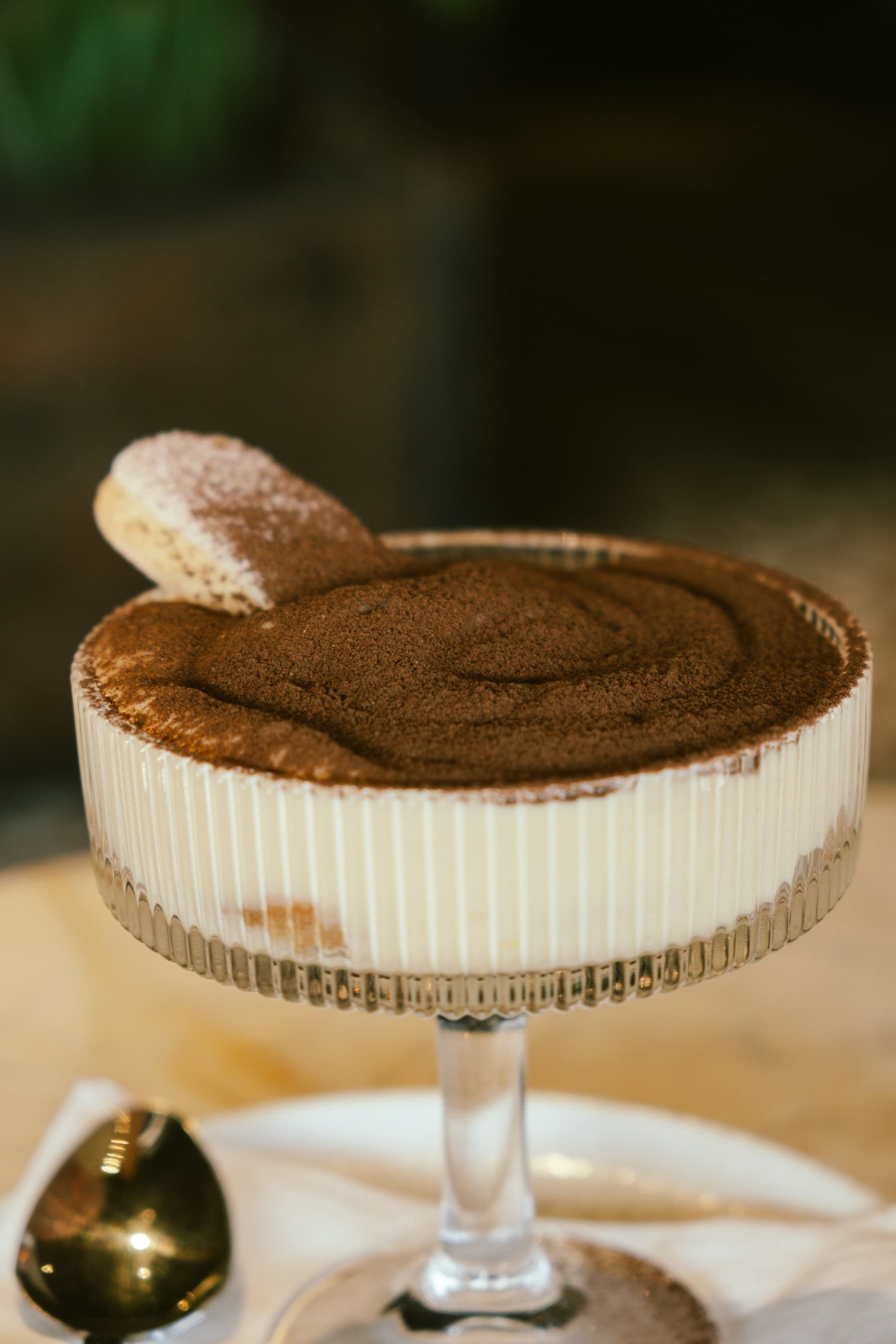 Tiramisù served in a fluted glass coupe, dusted with cocoa and crowned with a savoiardi biscuit