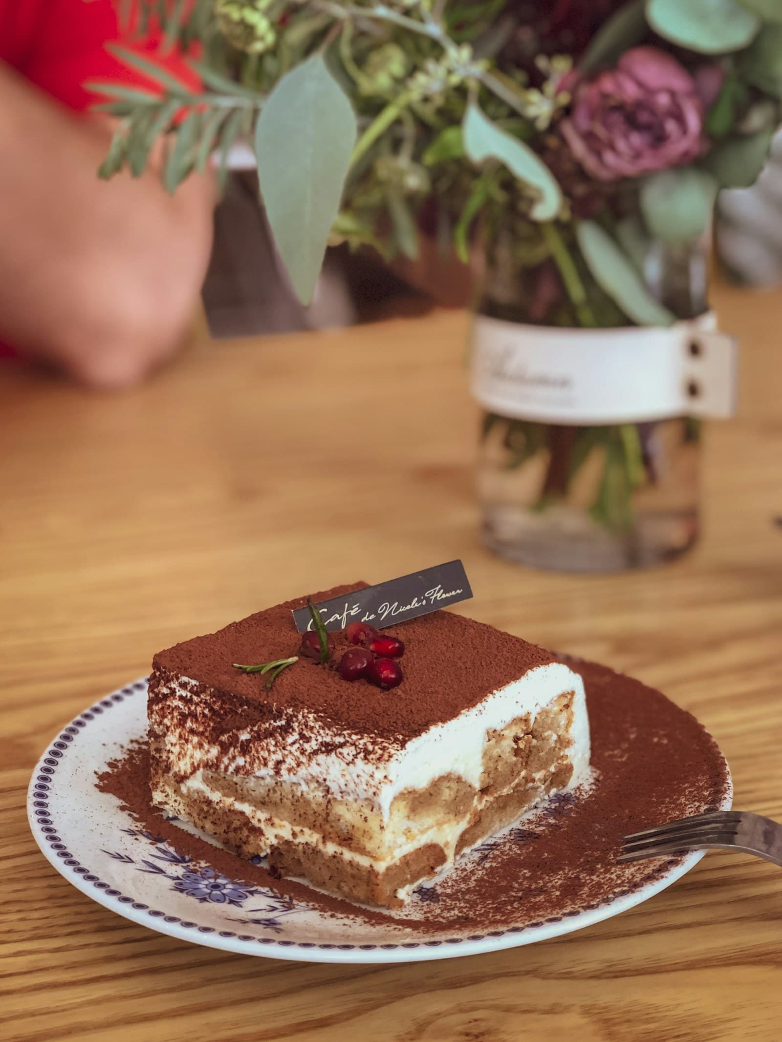 A slice of classic Tiramisù on a porcelain plate, dusted with cocoa, on a sunlit café table